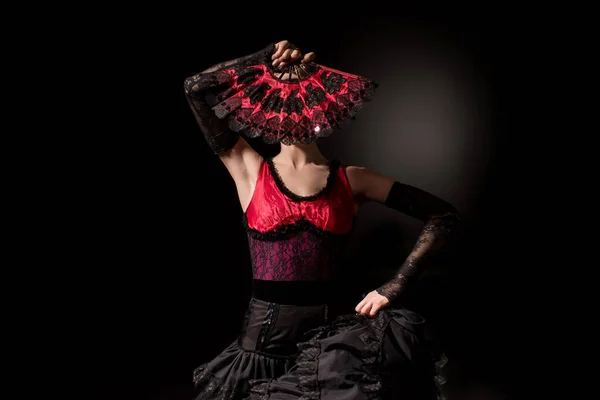 stock image young flamenco dancer in dress covering face with fan on black