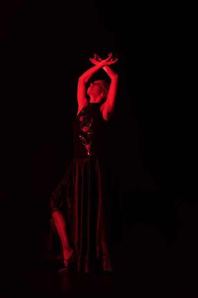 Красное освещение на привлекательную женщину с руками над головой танцует фламенко изолированы на черном
  