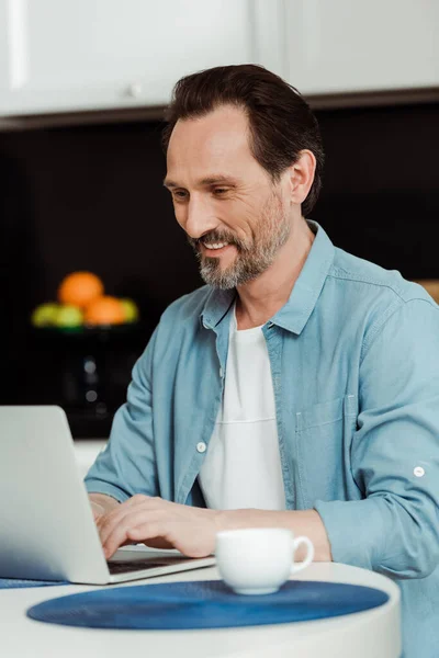 Enfoque Selectivo Del Hombre Sonriente Utilizando Ordenador Portátil Cerca Taza —  Fotos de Stock