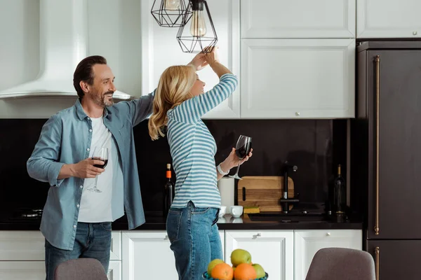 キッチンでワイングラスと陽気な成熟したカップルダンスの選択的な焦点 — ストック写真