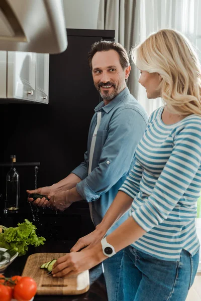 Vista Lateral Del Hombre Sonriente Mirando Esposa Cortando Pepino Cocina — Foto de Stock