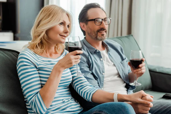 Leende Mogna Par Som Håller Händer Och Dricker Vin Soffan — Stockfoto