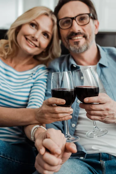 有选择地把焦点放在微笑的成熟夫妻手牵着手 在家里和葡萄酒叮当作响上 — 图库照片