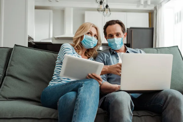 Mature Couple Medical Masks Using Gadgets Sofa Home — Stock Photo, Image