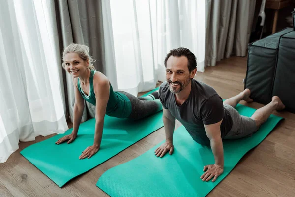 Lachend Volwassen Koppel Kijkend Naar Camera Terwijl Thuis Trainen Fitnessmatten — Stockfoto