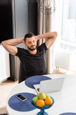 Sakallı serbest çalışan akıllı telefonun yanındaki masadaki boş ekran bilgisayara bakıyor.