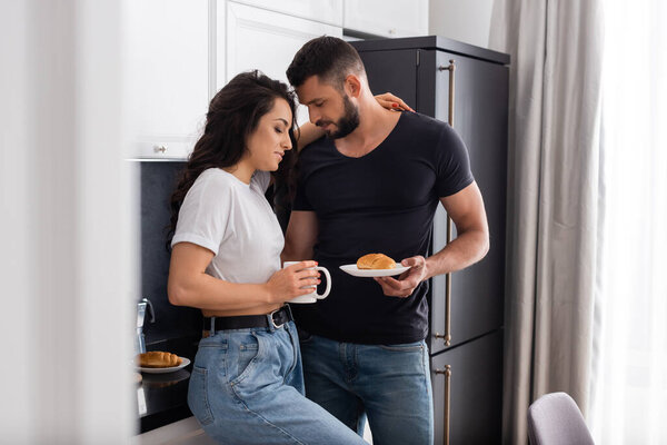 selective focus of bearded man holding croissant on plate near girl with cup 