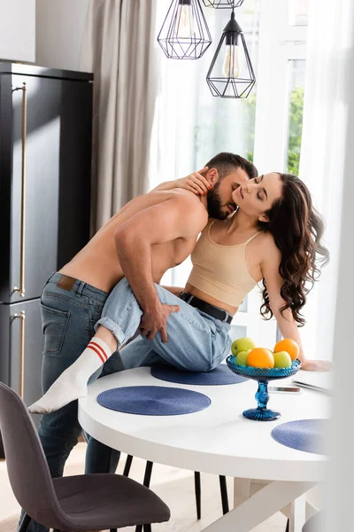 裸男亲吻坐在桌子上的充满热情的女孩的选择性焦点 — 图库照片