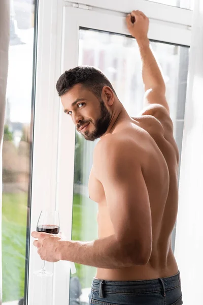 muscular and bearded man holding glass of red wine