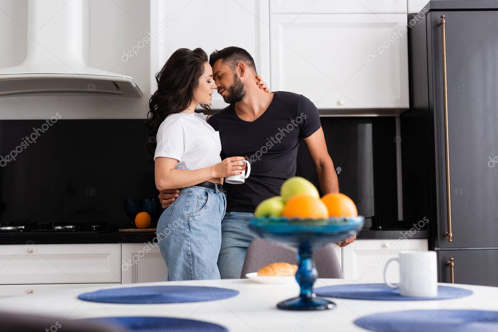 selective focus of beautiful woman holding cup and standing with boyfriend in kitchen 