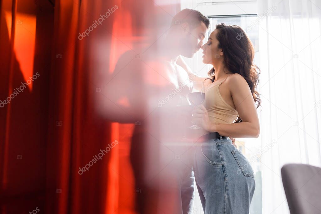 selective focus of muscular man holding glass of red wine near attractive girl in jeans 