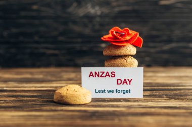 card with anzas day lettering near artificial flower and cookies on wooden surface  clipart