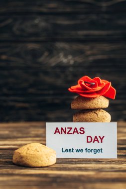 card with anzas day lettering near artificial flower and tasty cookies on wooden surface  clipart