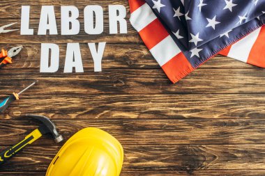 Enstrümanların yanındaki Amerikan bayrağının en üst görüntüsü, güvenlik kaskı ve tahta yüzeydeki işçi günü harfleri. 
