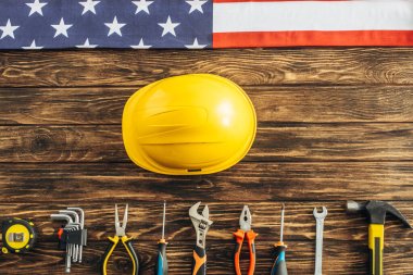 Metalik aletlerin üst görüntüsü, güvenlik kaskı ve ahşap yüzeyde Amerikan bayrağı, İşçi Bayramı konsepti 