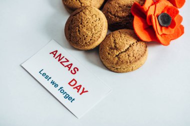 card with anzas day lettering near artificial flower and cookies on white clipart