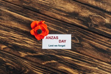 top view of artificial flower near card with anzas day lettering on wooden surface  clipart