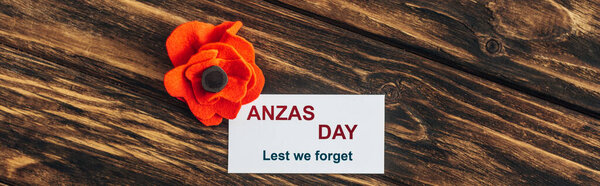panoramic shot of card with anzas day lettering near artificial flower on wooden surface 