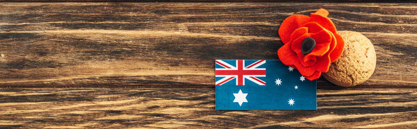 panoramic crop of australian flag near artificial flower and cookie on wooden surface 