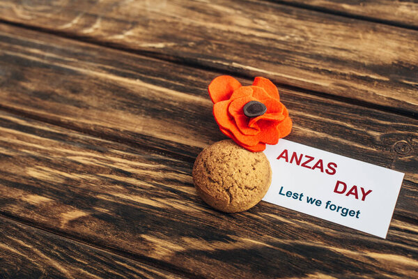 card with anzas day lettering near artificial flower and cookie on wooden surface 