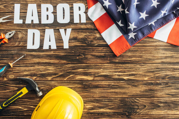 top view of american flag near instruments, safety helmet and labor day lettering on wooden surface 