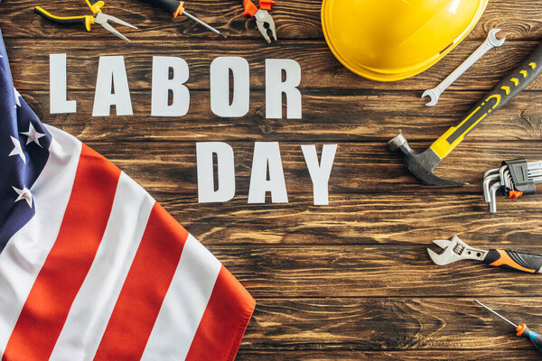 top view of american flag near tools, safety helmet and labor day lettering on wooden surface 