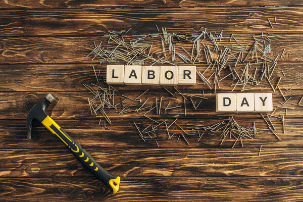 верхний вид металлических гвоздей и молотка возле кубов с надписью трудового дня на деревянной поверхности

