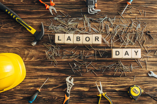 top view of metal nails, safety helmet and instruments near cubes with labor day lettering on wooden surface