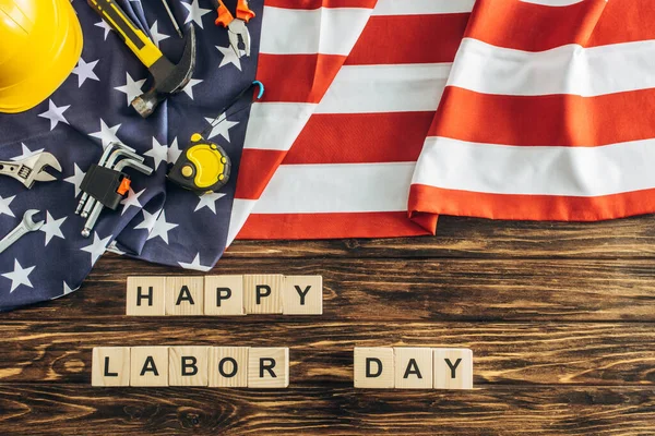 top view of instruments and safety helmet near happy labor day lettering on american flag and wooden surface