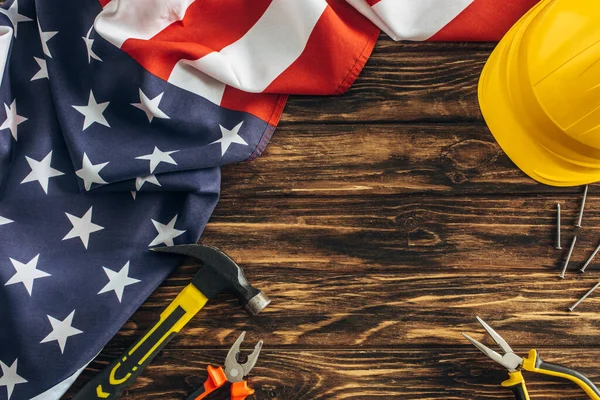 Tahta yüzey üzerinde Amerikan bayrağının ve güvenlik kaskının yanındaki aletlerin üst görüntüsü, İşçi Bayramı konsepti 