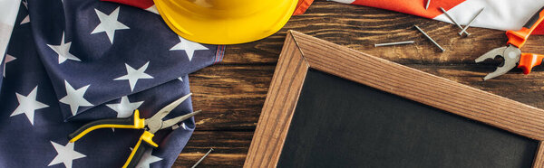 panoramic crop of american flag and instruments near blank chalkboard on wooden surface, labor day concept 