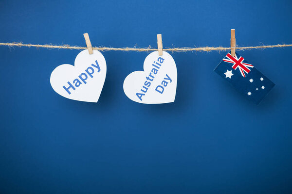 rope, clothespins and heart-shaped papers with happy near australia day lettering and flag on blue