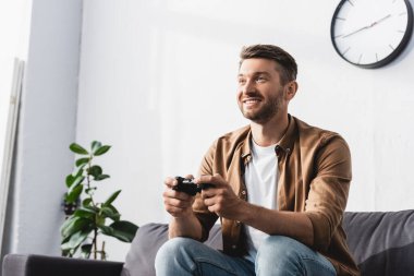 KYIV, UKRAINE - 9 Haziran 2020: Kanepede oturan ve joystick ile video oyunu oynayan neşeli adam