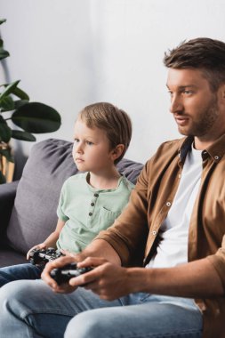 KYIV, UKRAINE - 9 Haziran 2020: koltukta oturup joysticklerle video oyunu oynayan baba ve oğul