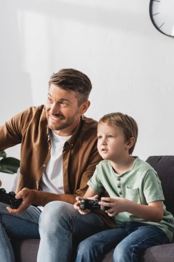 KYIV, UKRAINE - 9 Haziran 2020: joysticklerle video oyunu oynayan heyecanlı baba ve oğul