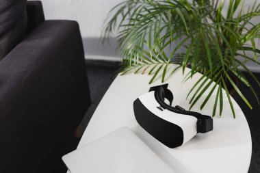 virtual reality headset and closed notebook near green plant on table