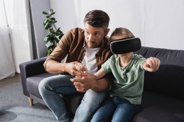 Baba, vr kulaklık kullanırken oğlunun ellerine dokunuyor.