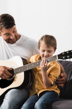 Mutlu baba, sevimli, gülümseyen oğlana akustik gitar çalmayı öğretiyor.