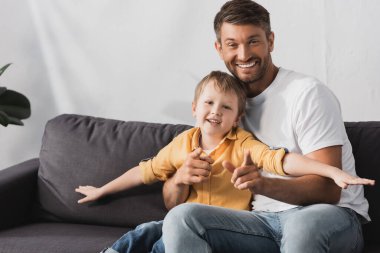 Mutlu baba ve gülümseyen oğul ellerini uzatmış evde koltukta oturuyor.