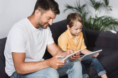 Evde dijital tablet kullanan gülümseyen baba ve özenli oğlun seçici odağı