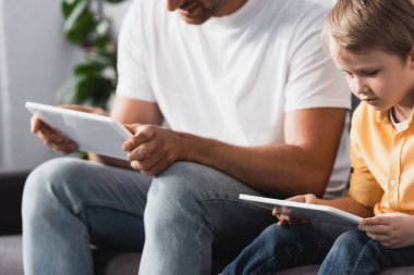 Evde dijital tablet kullanan baba ve oğulun kesilip biçilmiş görüntüsü.