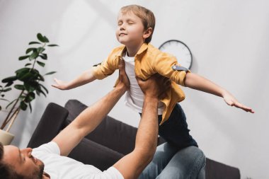 Baba yerde yatar ve tapılası oğlu kapalı gözlerle uçar.