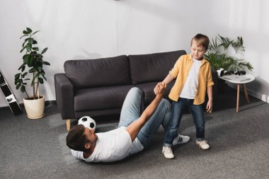 Sevimli çocuk elinde futbol topu tutan babaya el uzatıyor.