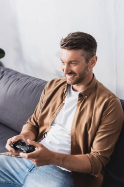 KYIV, UKRAINE - 9 Haziran 2020: Mutlu, yakışıklı adam kanepede oturuyor ve joystick ile video oyunu oynuyor