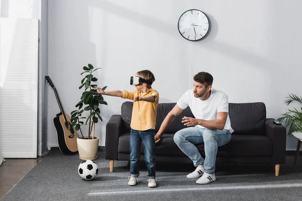 Boy Headset Standing Outstretched Hands Father Sitting Sofa — Stock Photo, Image