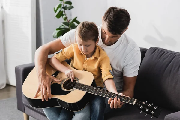 Cute Boy Sitting Fathers Knees Learning How Play Acoustic Guitar — Stock Photo, Image
