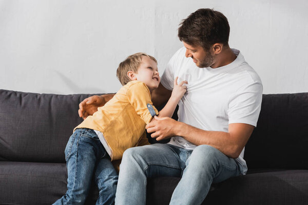 cheerful father and son having fun while jokingly fighting on sofa at home