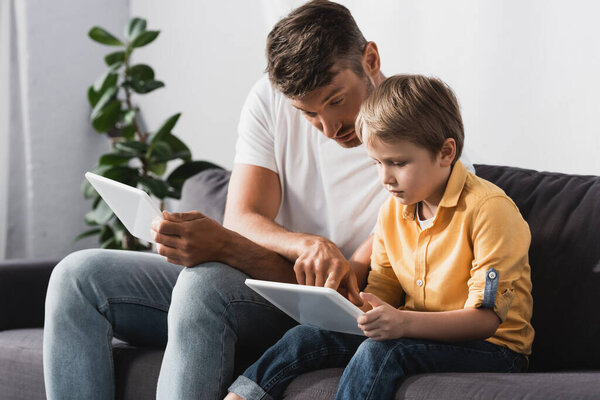 father pointing with finger at digital tablet in hands of adorable son