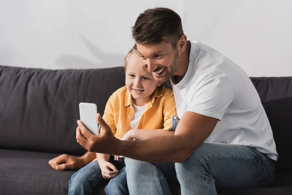 Sorrindo Pai Filho Tomando Selfie Smartphone Enquanto Sentado Sofá — Fotografia de Stock