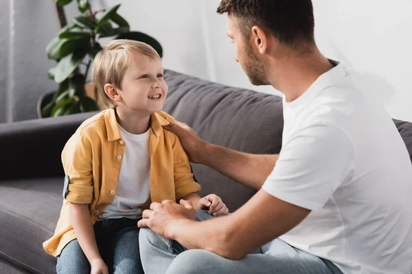 Father Touching Shoulder Smiling Son While Talking Him Sofa — Stock Photo, Image